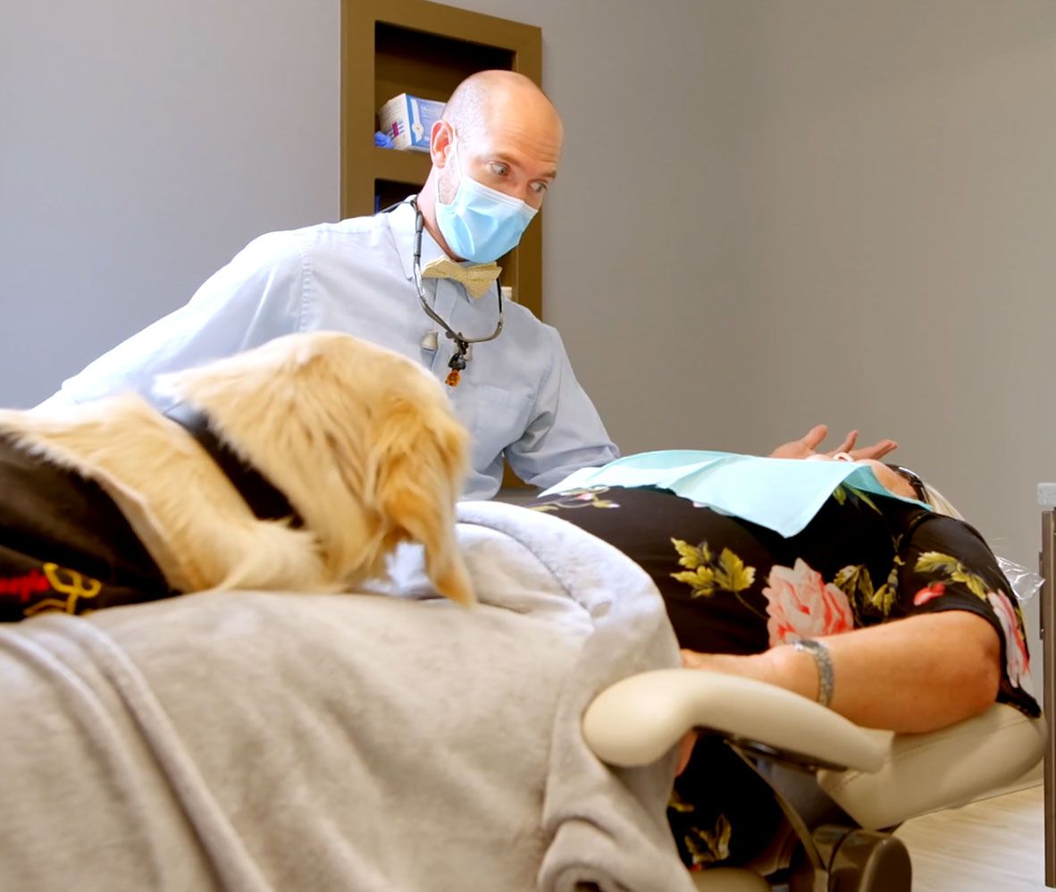 Dentist treating a patient with a therapy dog nearby at Thrive Family Dental in Wilmington, NC